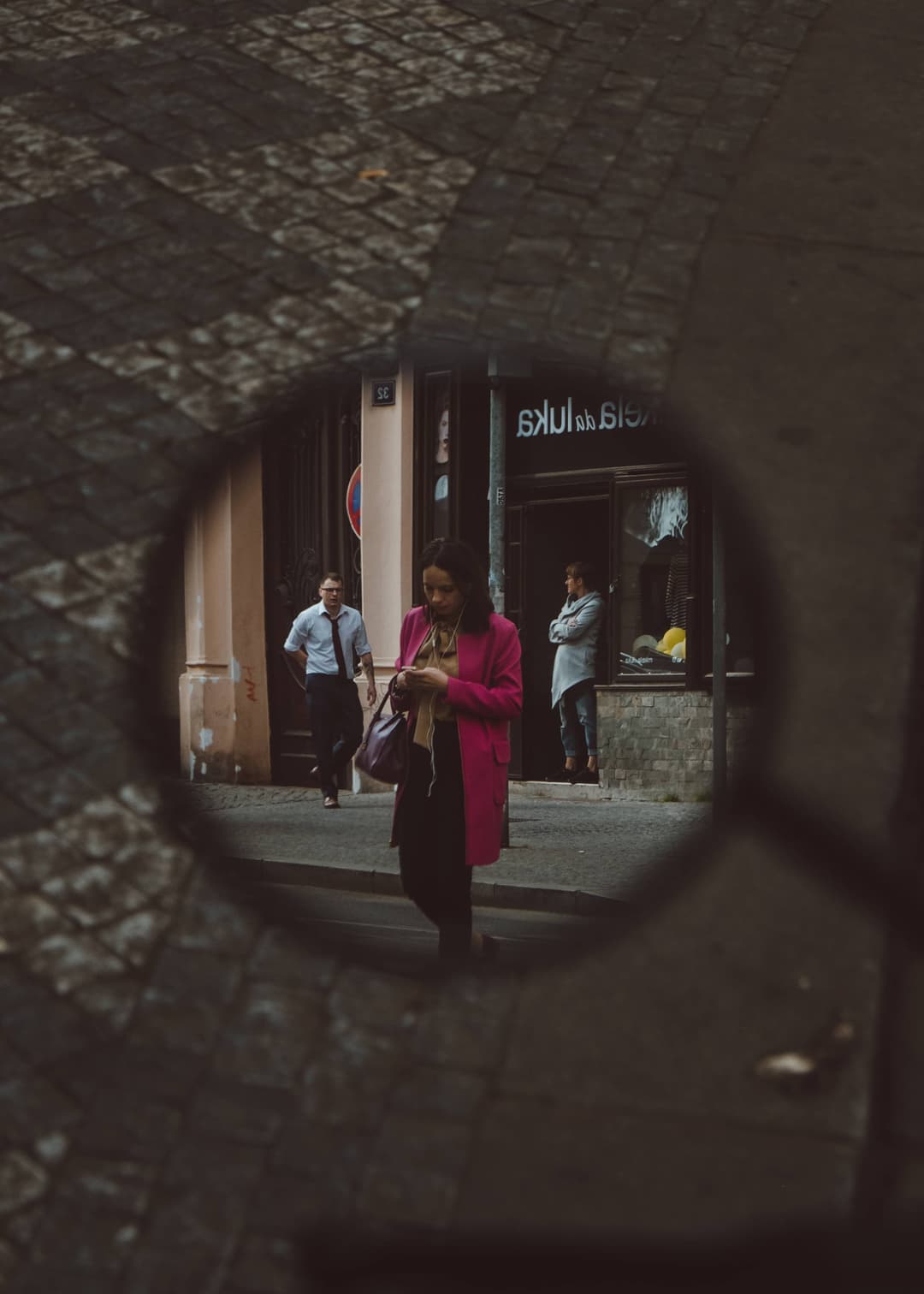 Mirror showing woman wearing pink coat walking on street