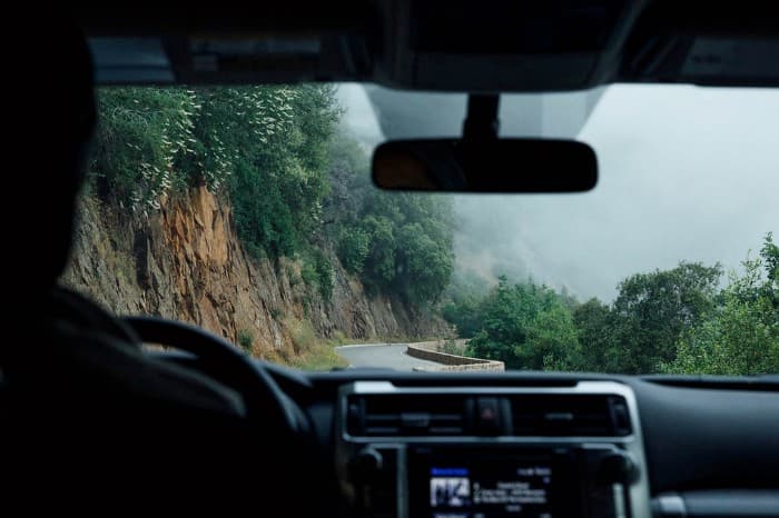 Looking out the windscreen of a car from the backseat, driving along on a narrow windy road