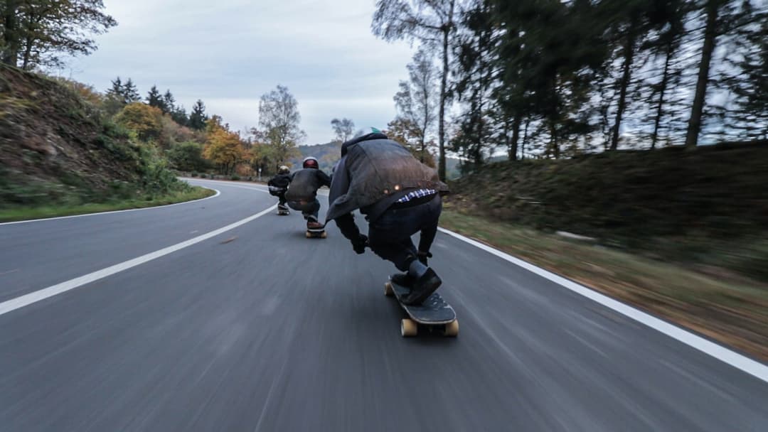 First person point of view of 3 people in front skating down downhill on boards