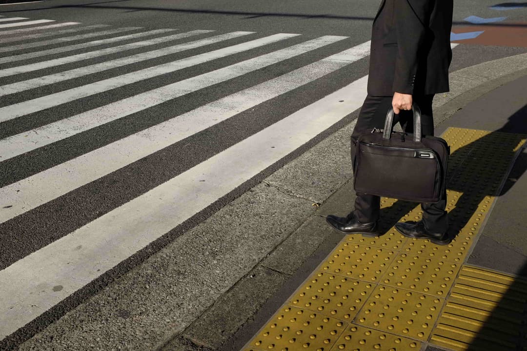 Man in a suit holding a briefcase about to cross a zebra crossing