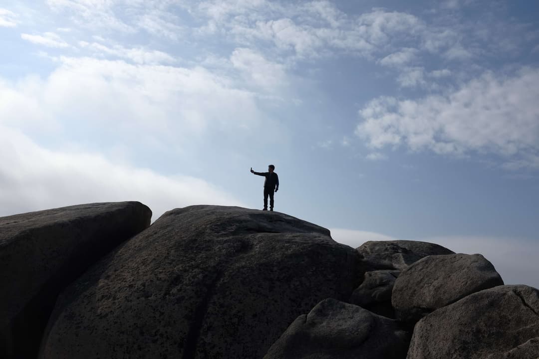 Man standing on a huge boulder taking a selfie